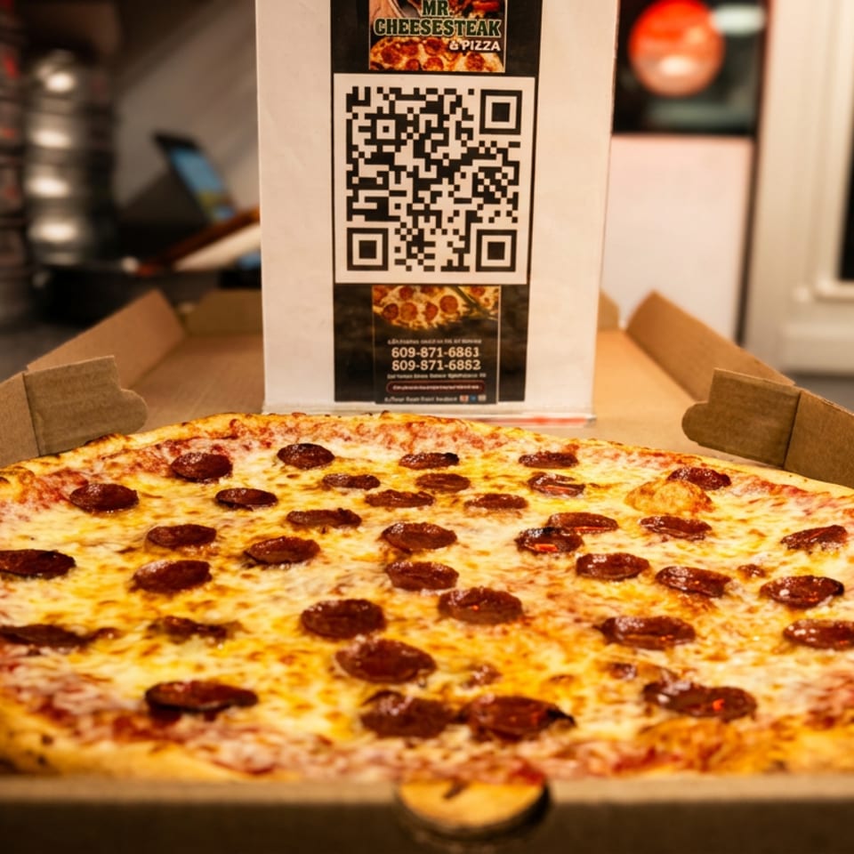 Pepperoni pizza in an open cardboard box on a restaurant counter, with Mr. Cheesesteak & Pizza signage behind it.